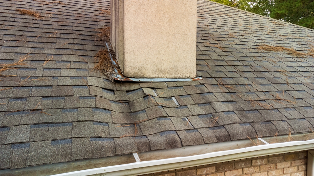 Roof with warped shingles and debris around the base of a chimney indicating possible water damage.