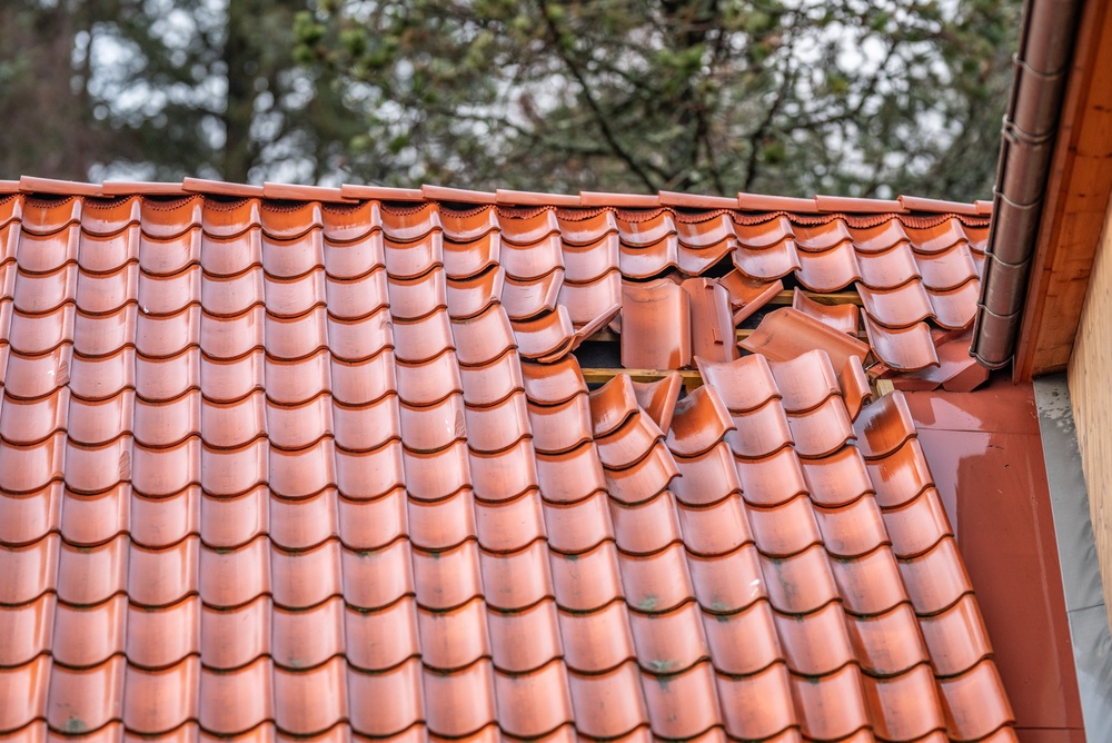 Red clay roof tiles with a section of broken and displaced tiles near the edge.
