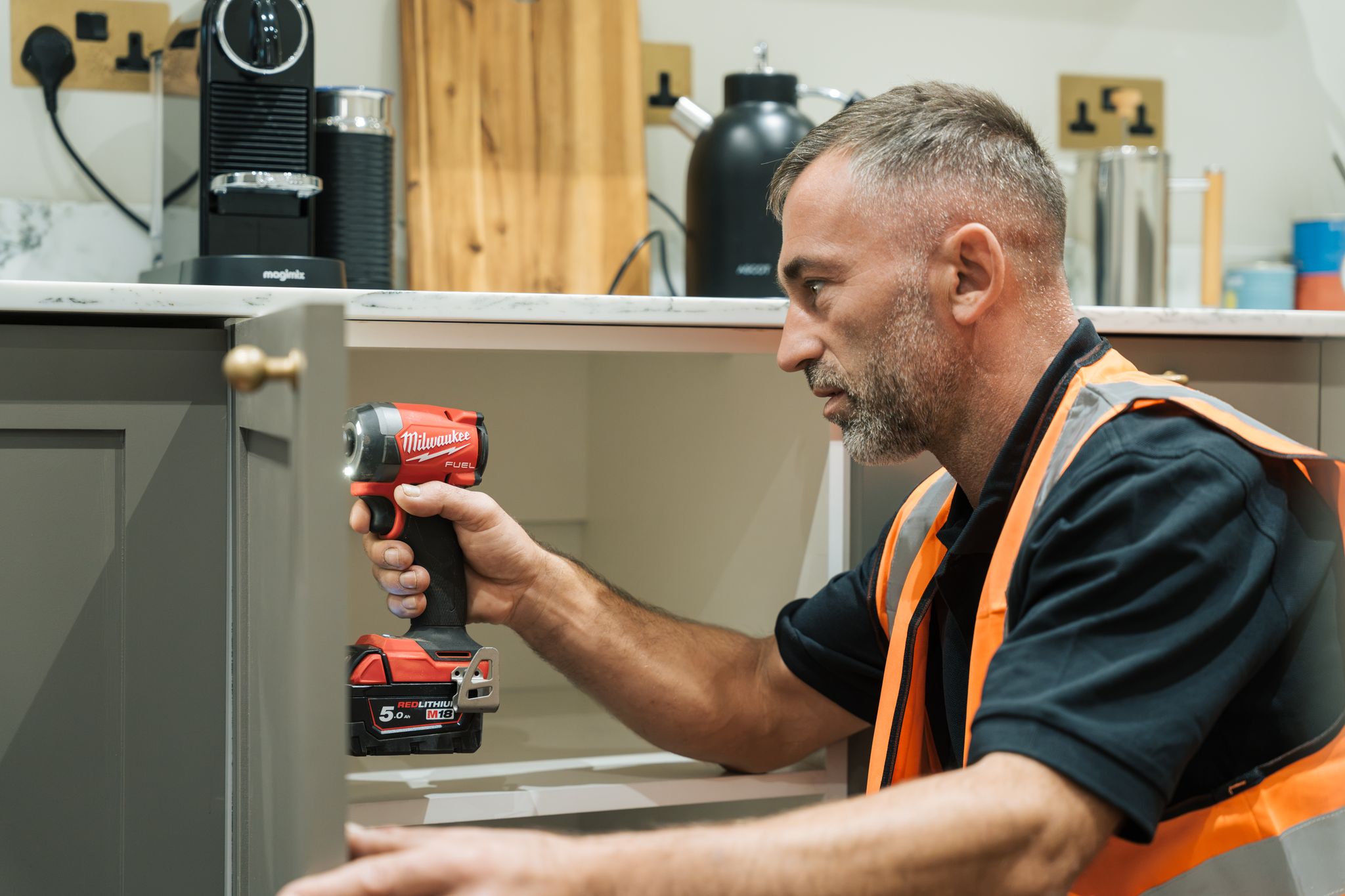 Man with beard applying plaster or paint on wall near decorative molding wearing a black glove.