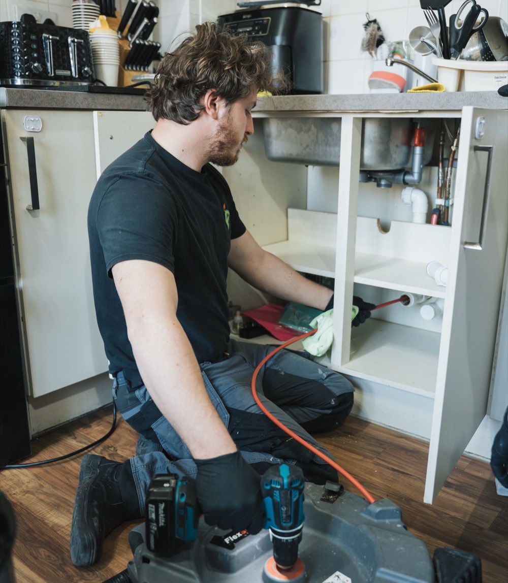 FS Group engineer kneeling at a kitchen unit with a drain clearing machine
