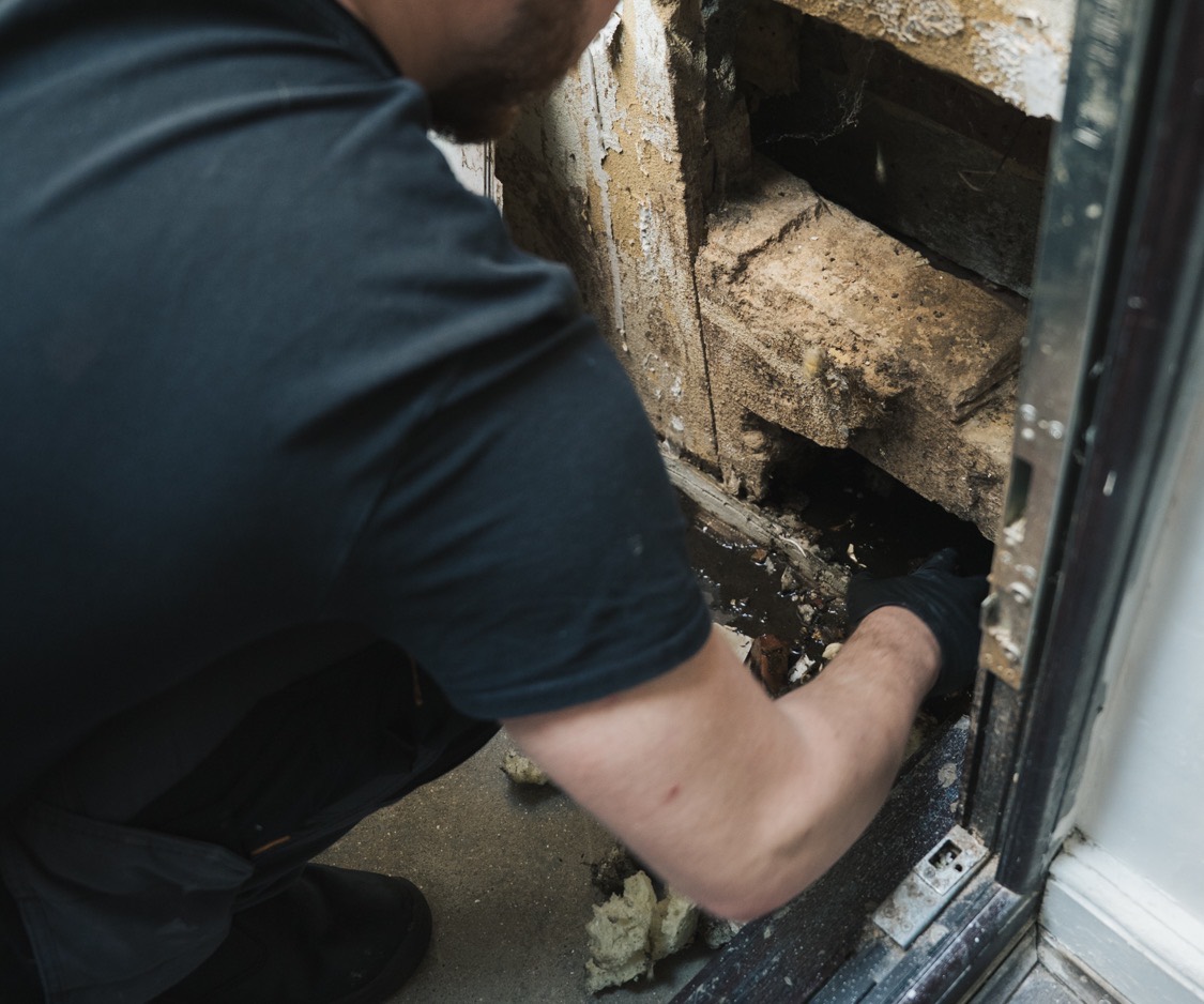 FS Group engineer working at a drain access point behind a door