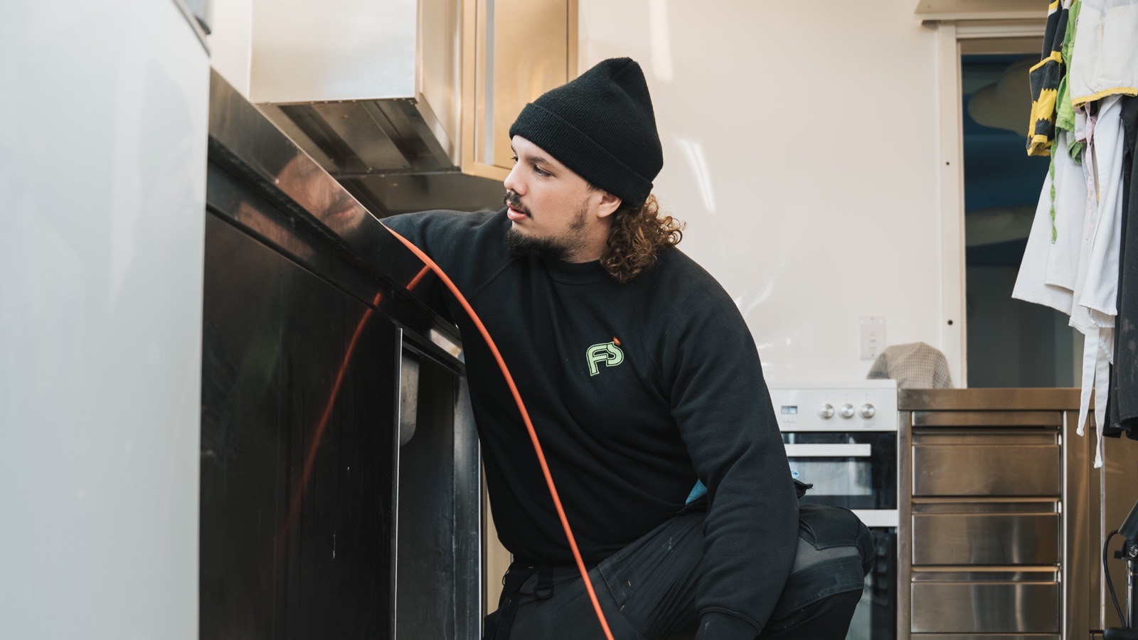 FS Group engineer feeding a drain cable under a commercial kitchen counter