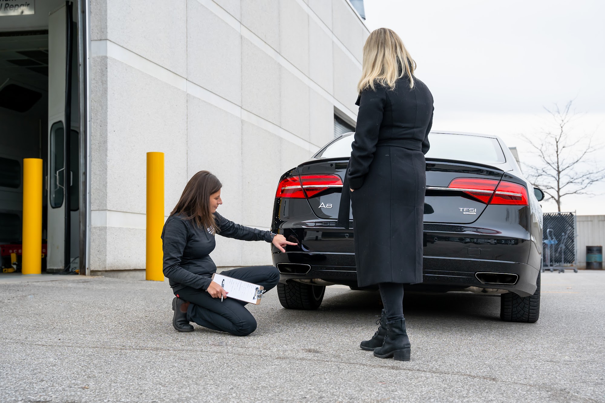 A CSN Avenue Collision estimator with a clipboard inspects the rear of a black Audi with its owner