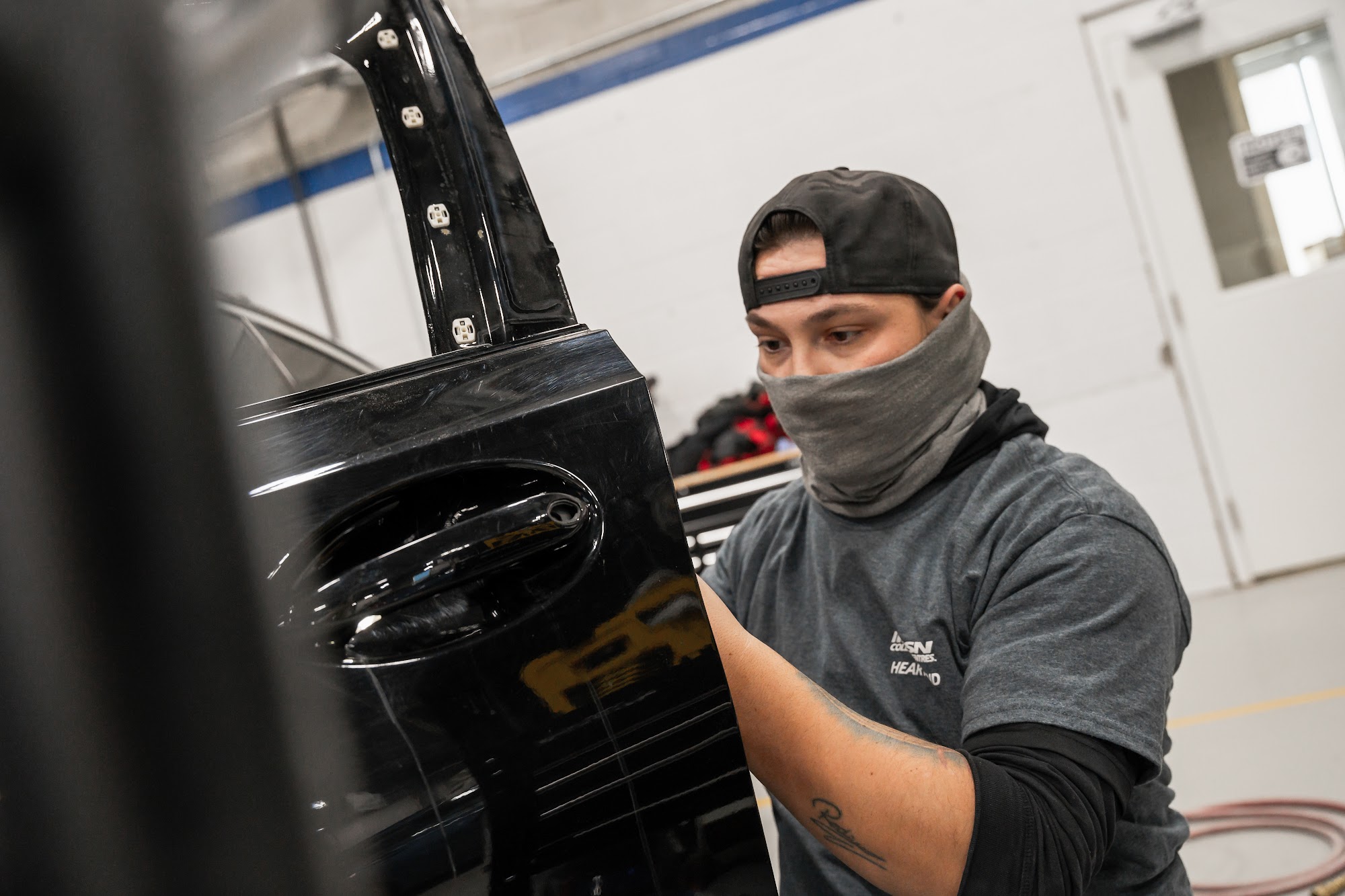 A CSN Avenue Collision technician works on a black door panel removed for refinishing