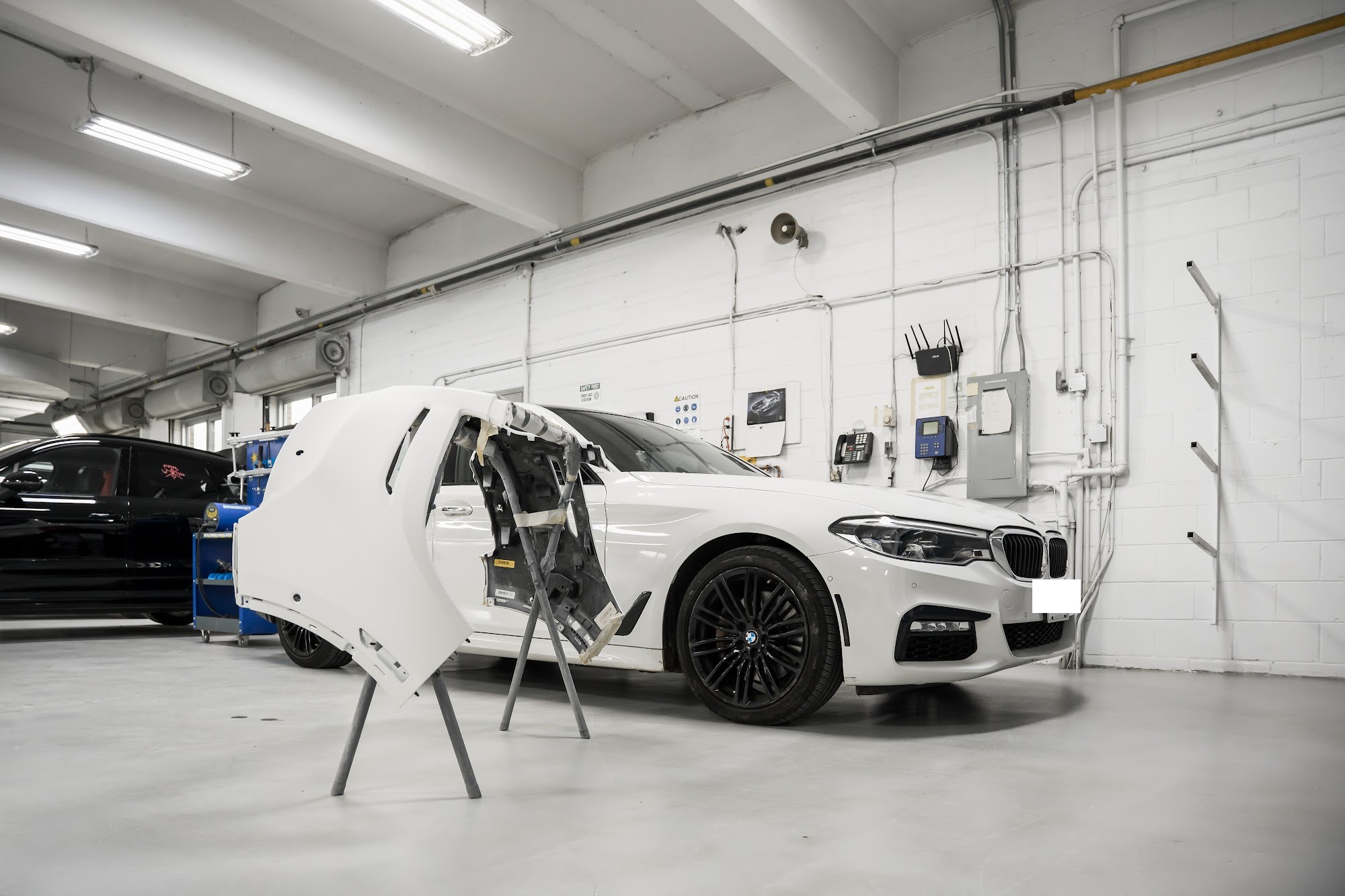 White BMW 5 Series mid-repair on the CSN Avenue Collision shop floor with its door panel on a stand
