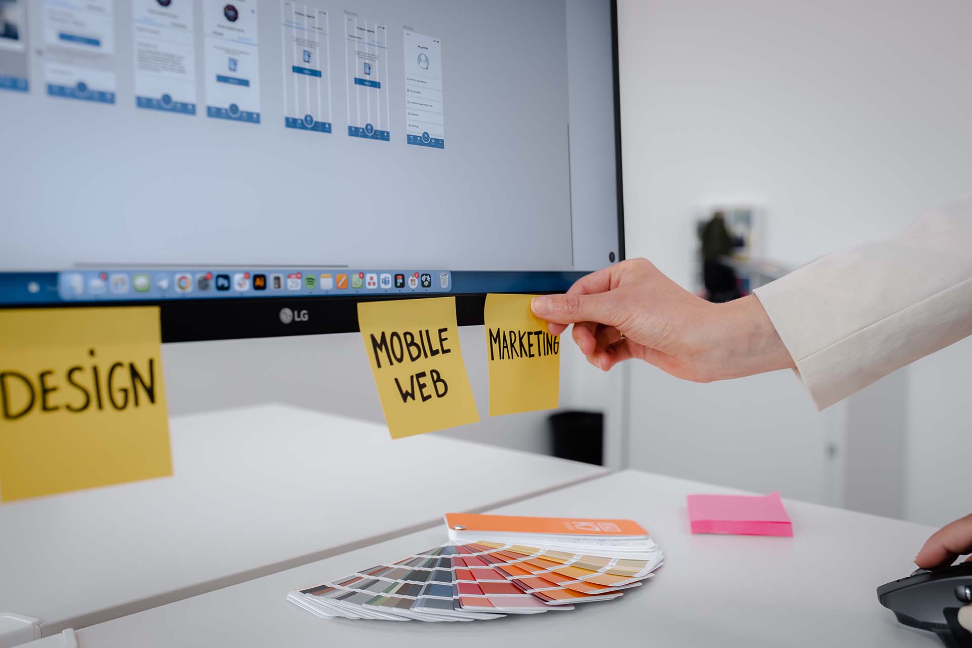 A person sticking a note sticker with the text Marketing on a desktop monitor