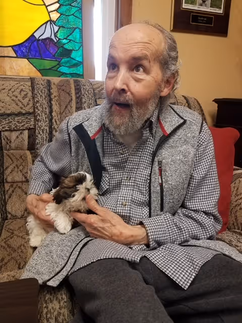 A man sitting on a couch holding a small dog
