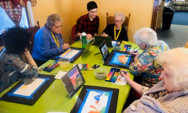 A group of people sitting around a table with paintings on it