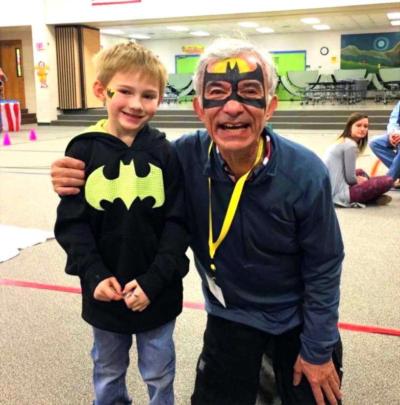 Young boy and older man dressed as Batman characters, smiling in school gymnasium.