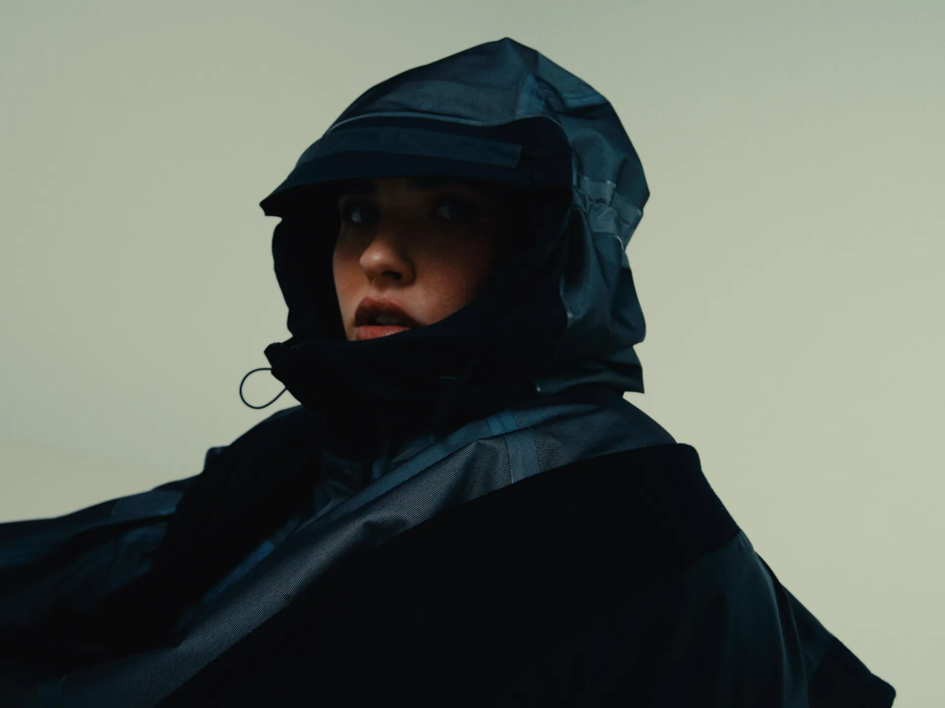 Portrait of a person wearing a black rain jacket with the hood up against a plain background.