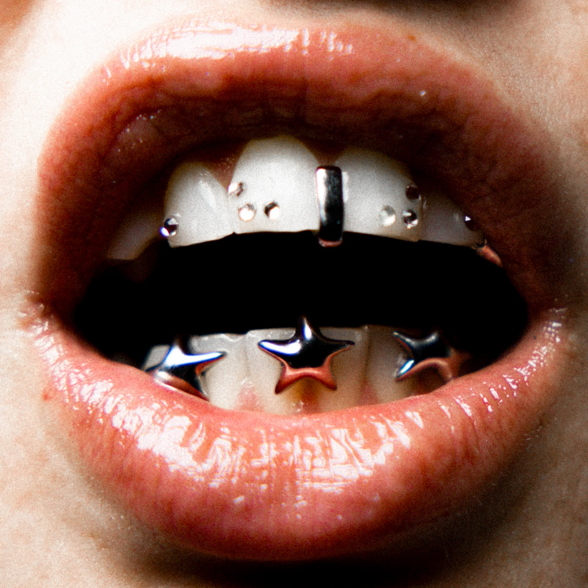 Close-up of open lips showing teeth adorned with star-shaped and small round metallic dental jewelry.