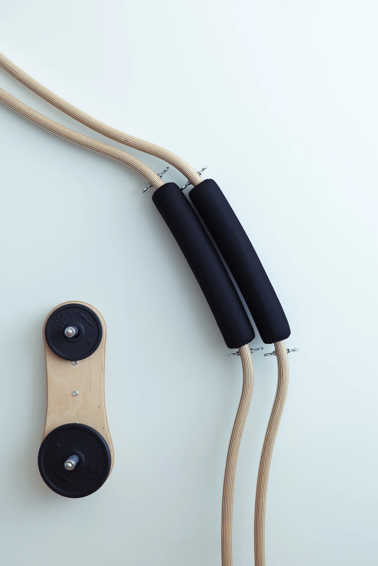 Wooden Pilates reformer spring cords with black padded handles and weight plates on the floor.