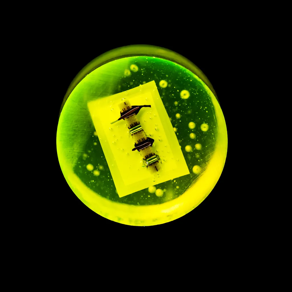 Technician in blue protective clothing and hairnet working on a complex industrial machine with metal hoses.