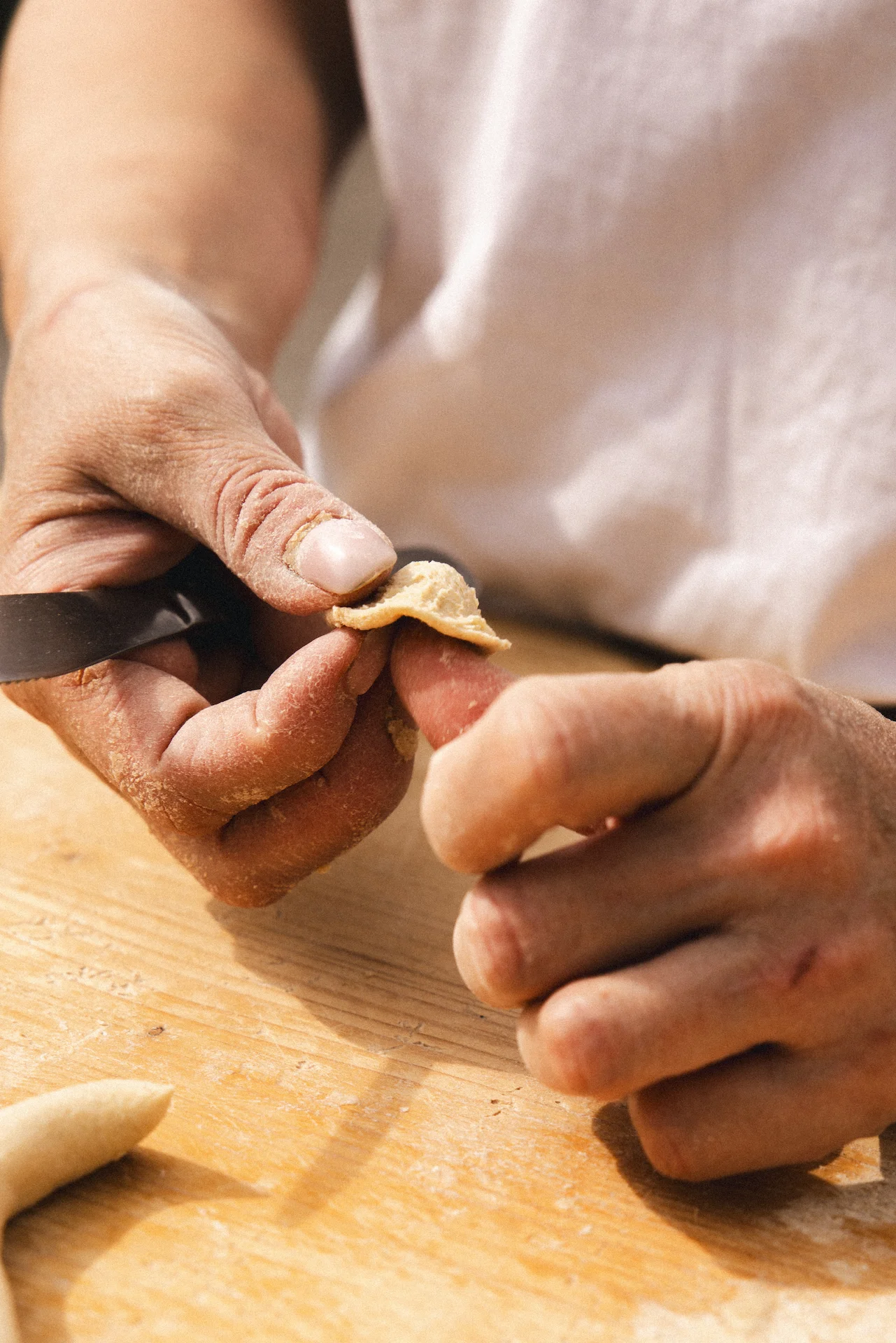 Close-up of hands shaping fresh pasta dough on a wooden surface.