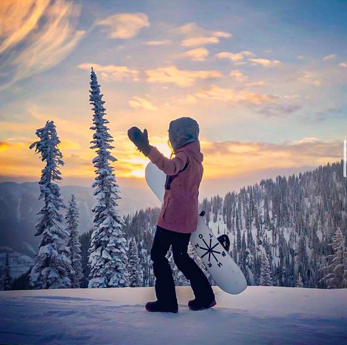 Resorts of the Canadian Rockies (RCR) ambassador, Sophia Gould, walks with her snowboard on a ridge, taking in an incredible sunrise amongst frozen trees at Fernie Alpine Resort in British Columbia.