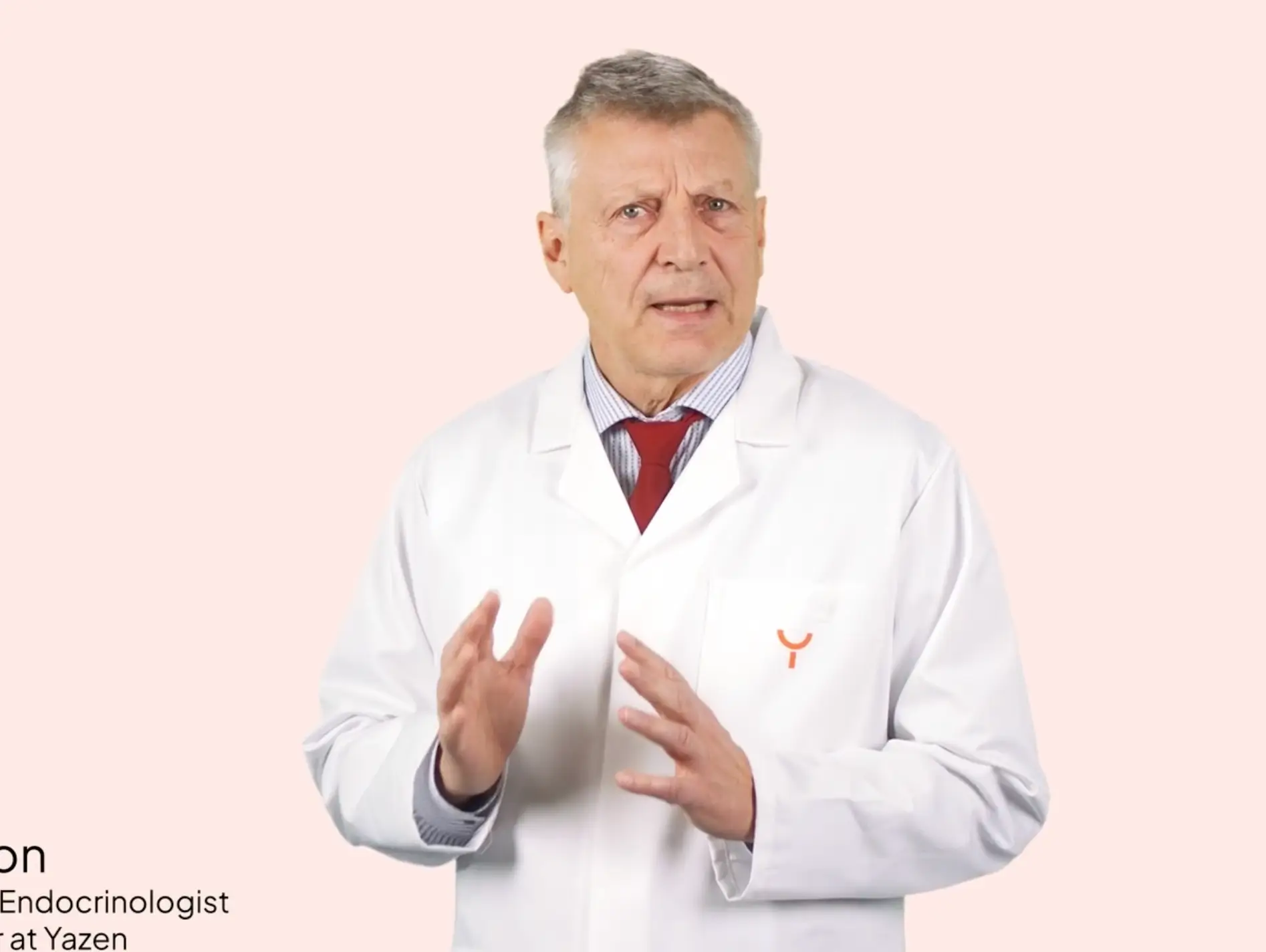 Middle-aged male doctor in white lab coat with red tie gesturing with his hands against a light pink background.