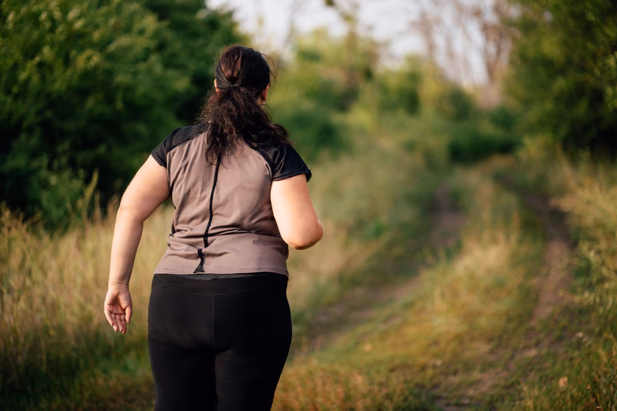 Woman jogging on a grassy path surrounded by green trees in an outdoor natural setting.