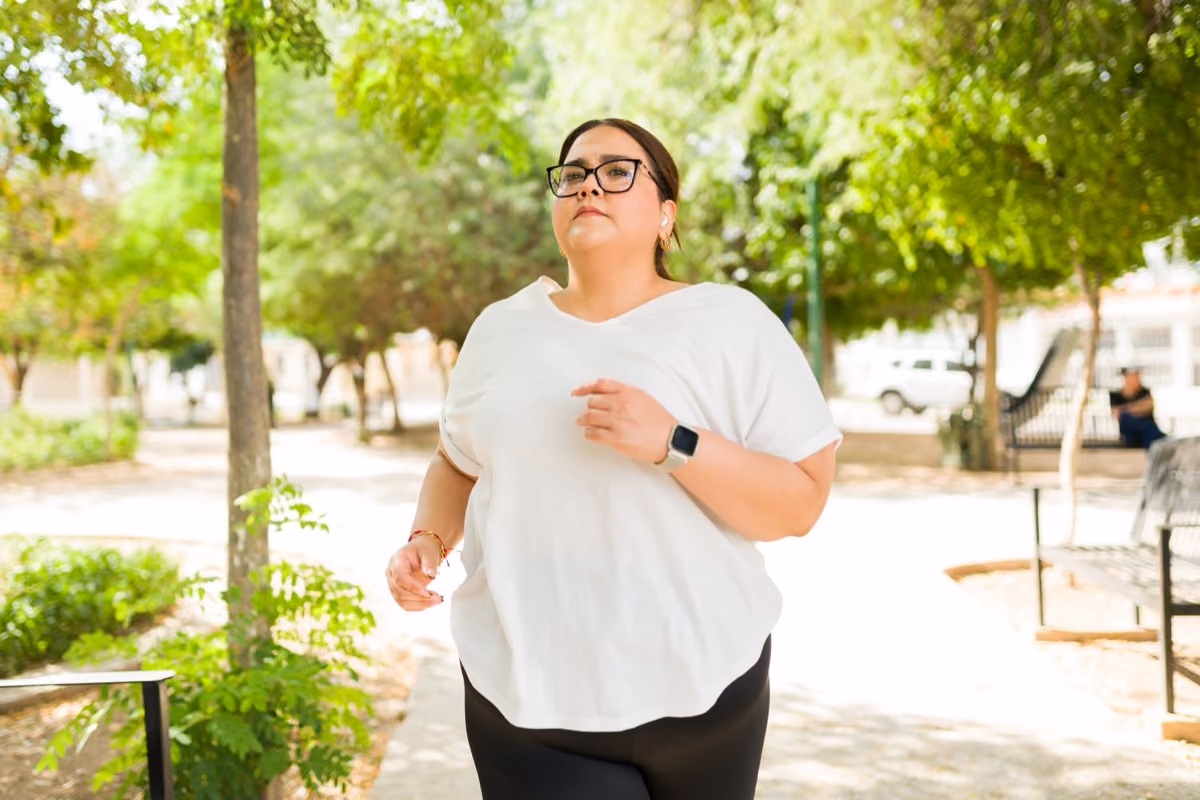 Woman jogging outdoors on a sunny day wearing glasses, white shirt, and black pants.