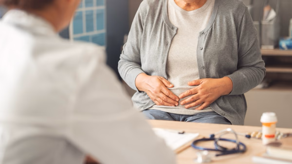 Woman in gray sweater holding her stomach during a consultation with a doctor.