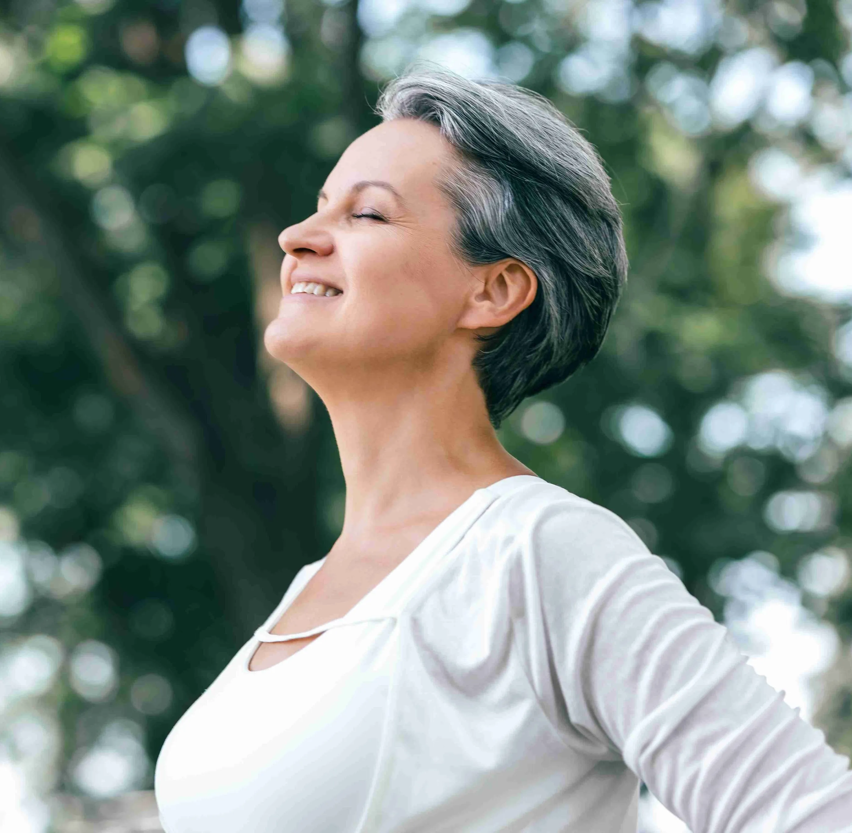 Smiling middle-aged woman with short gray hair enjoying fresh air outdoors with eyes closed.