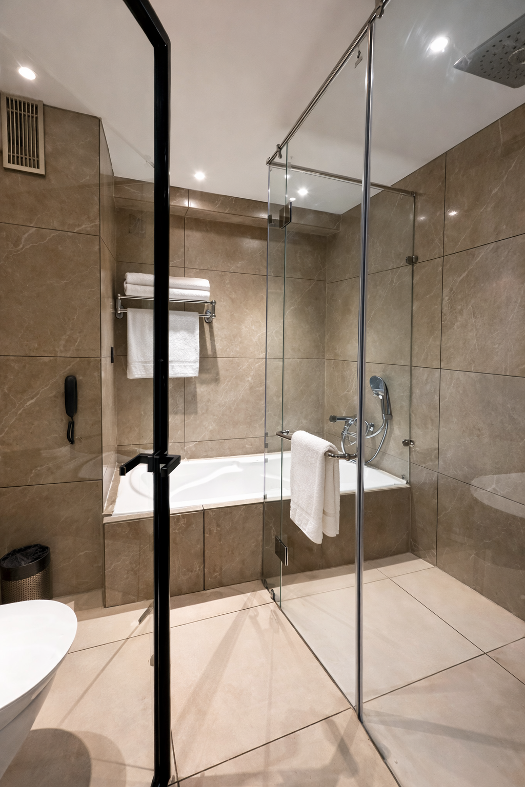 Modern bathroom with a glass-enclosed shower area, bathtub, beige tiles, and white towels.