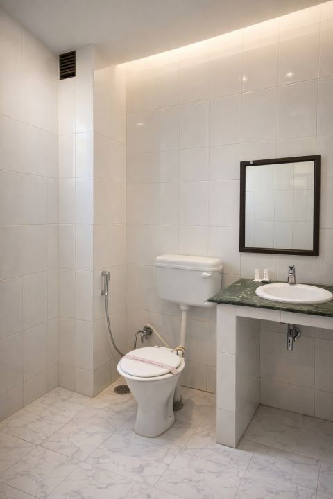 Clean bathroom with white tiled walls and floor, a toilet with a bidet spray, a green countertop with a sink, and a rectangular mirror above it.