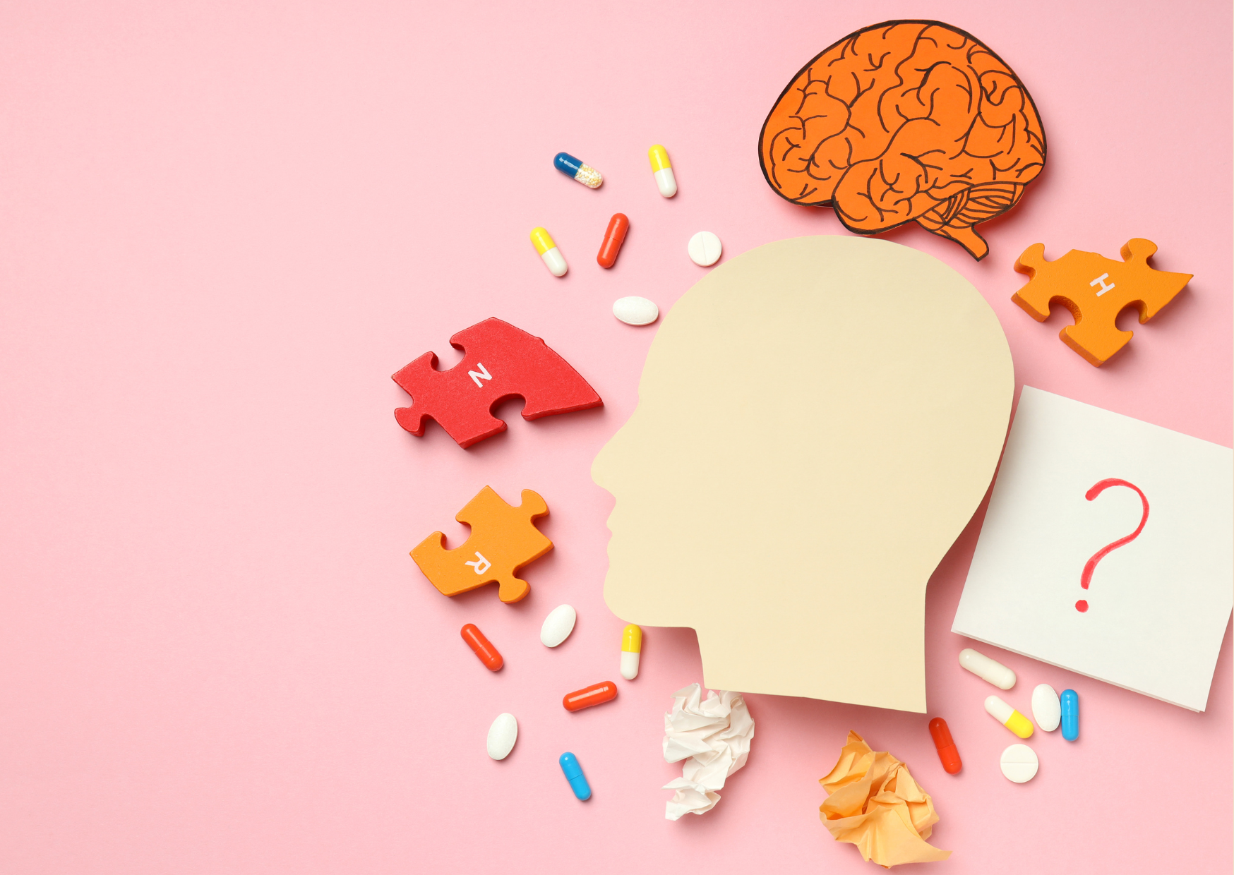 An image of a mental health and cognitive function showing a human head silhouette, a brain illustration, colourful puzzle pieces, various pills, crumpled papers, and a question mark on a notepad, all on a pink background.