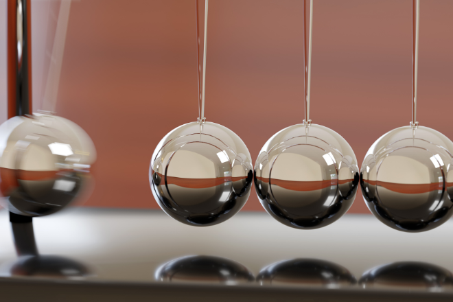One Metal ball lifted and in motion, about to strike the other metal balls. Image credit Canva.
