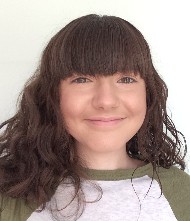 A brunette girl in front of a white background, smiling and wearing a green and white t-shirt.