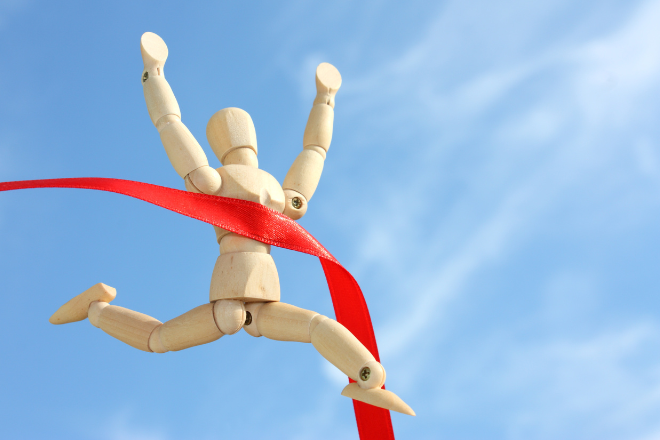 Wooden artist mannequin posed as a runner crossing a red finish line ribbon - Image credit Canva Pro 