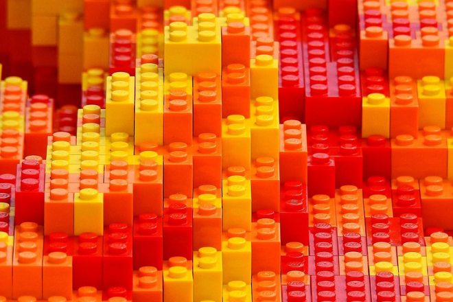 Close-up of stacked LEGO bricks in shades of red, orange, and yellow arranged in a dense, abstract pattern, creating a textured landscape of warm colors. - Photo by Bruno from Pixabay