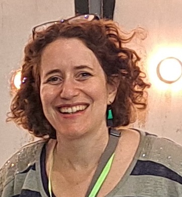 A photo of George, a white woman with shoulder-length curly hair and glasses on her hair. She is smiling at the camera.