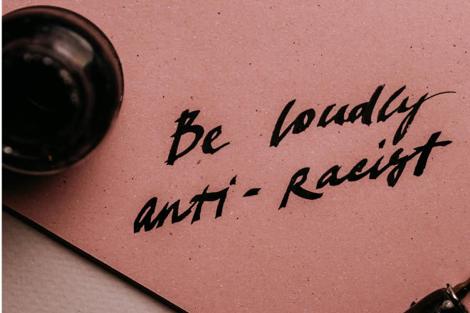Calligraphy writing on a pink background that says "Be loudly anti-racist"