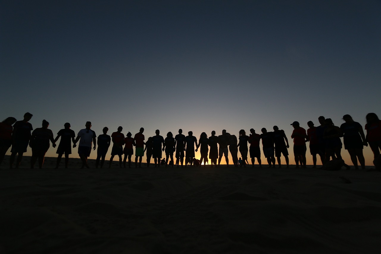 Silhouettes of a group of people standing in a semi-circle against a sunset.