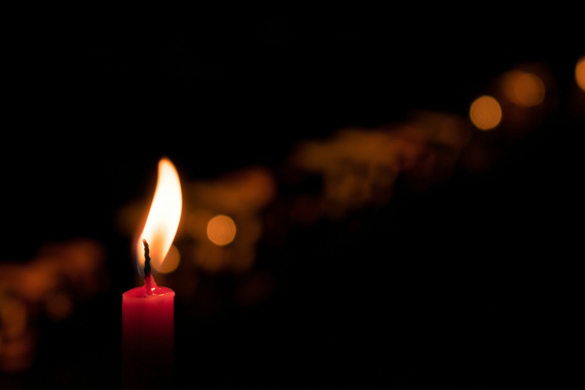 A red candle burning, surrounded by soft lights out of focus against a dark background.