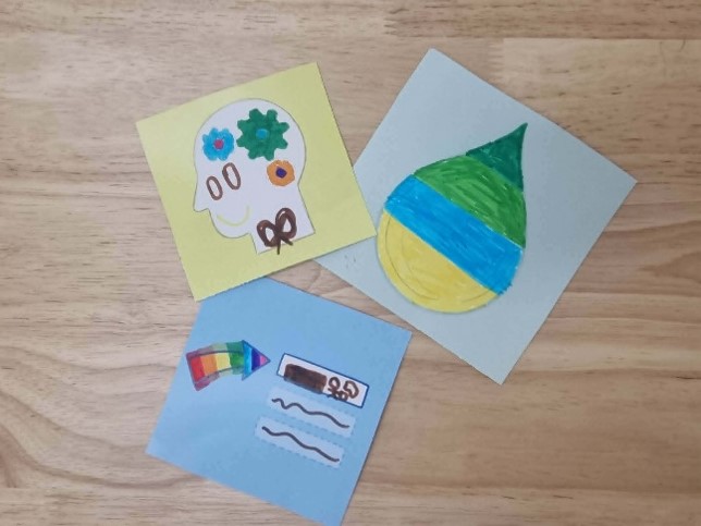 Three squares of coloured card featuring different hand drawn illustrations, including a head filled with cogs, a drop of water coloured in strpes, and a rainbow arrow pointing to three rectangles. 