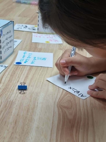 A child writing on a small piece of card using a felt-tip pen.