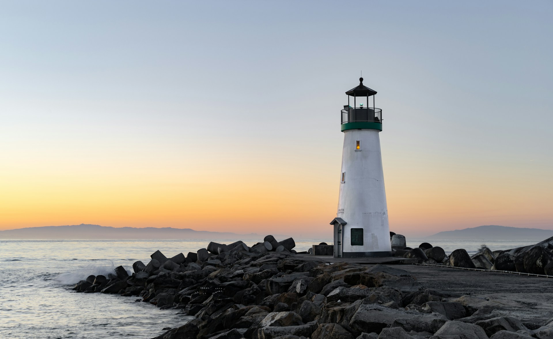 A white lighthouse on a rocky peninsula at sunrise
