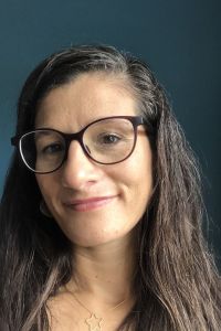 A photo of Maja's head and shoulders. Maja is a woman with long, dark brown hair and black glasses.