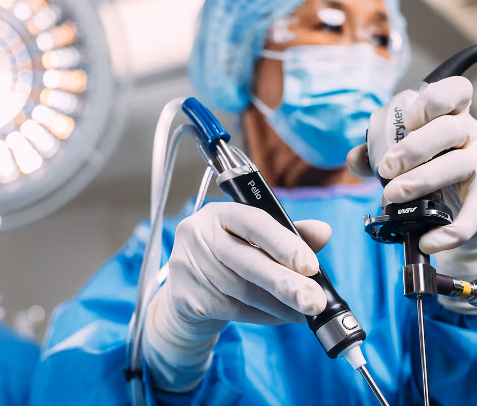 Surgeon in blue scrubs and mask holding advanced laparoscopic surgical instruments in an operating room.