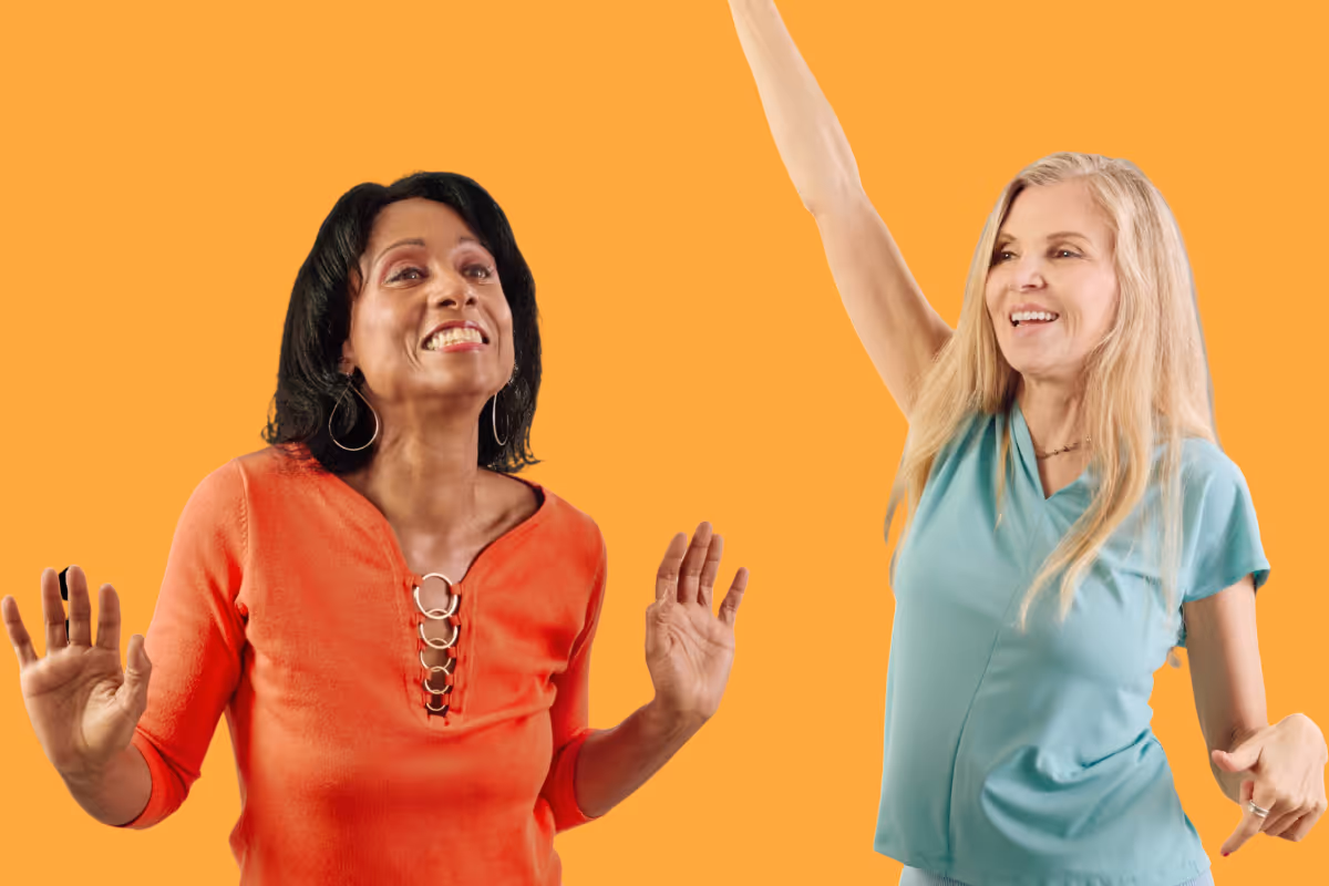 Two smiling women dancing, one in an orange top and the other in a light blue shirt, against an orange background.