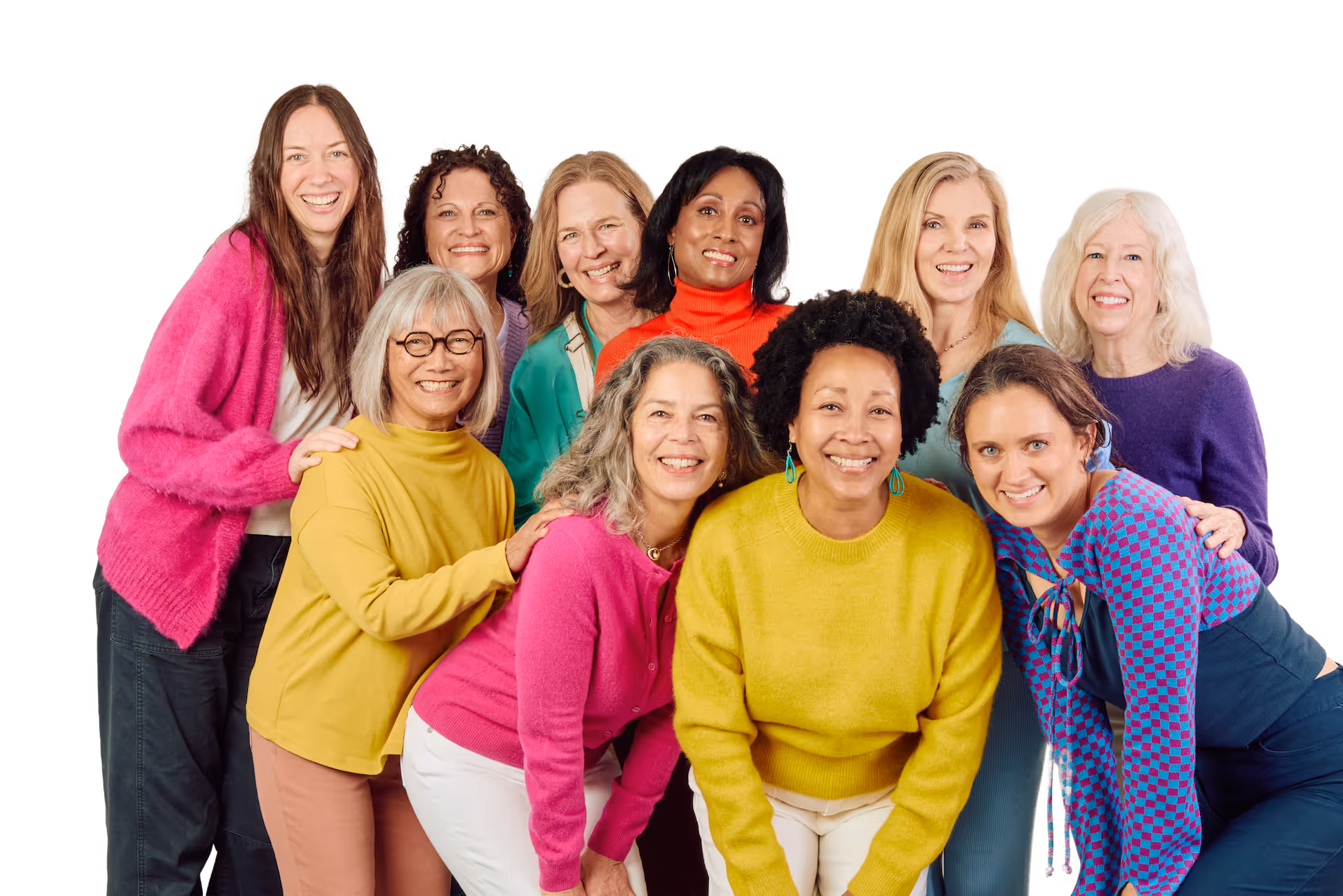 Group of ten diverse women smiling, wearing colorful sweaters, posing closely together against a black background.