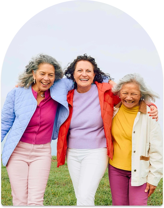 Three older women outdoors smiling and standing closely with arms around each other.