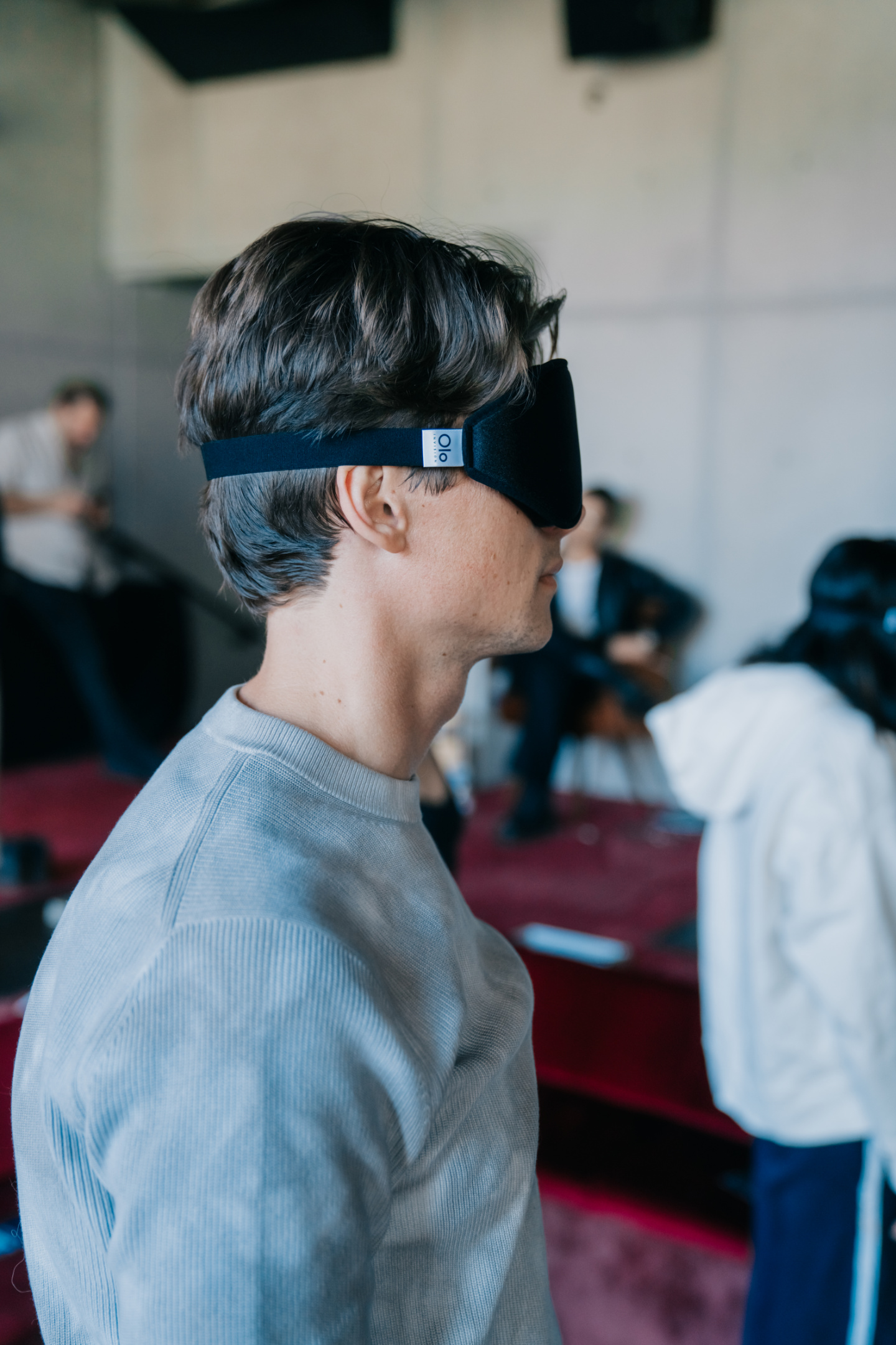 A man in profile wearing the Black Olo eye mask at a listening event