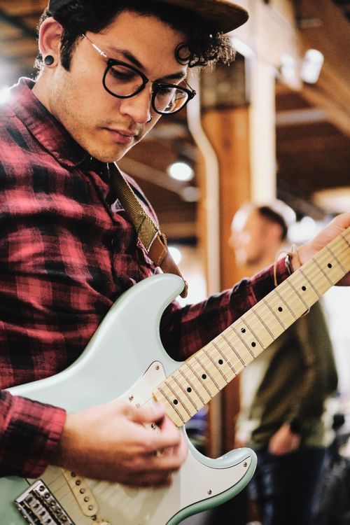Man with glasses and red flannel playing an electric guitar