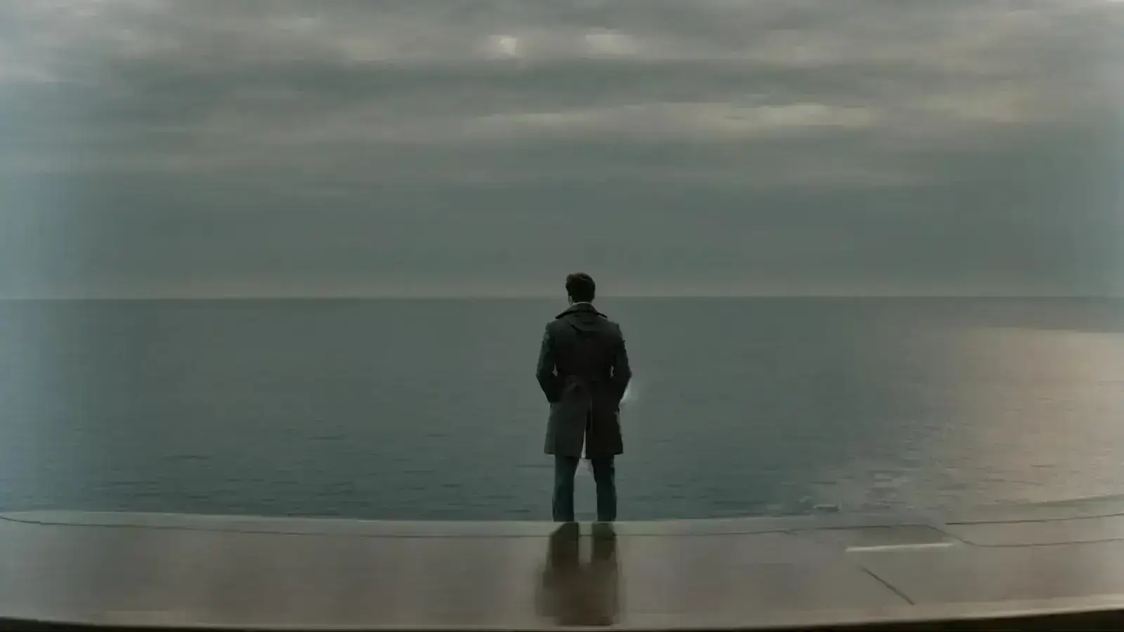 a person standing before a large ship's steering wheel, gazing out into a vast, open sea.