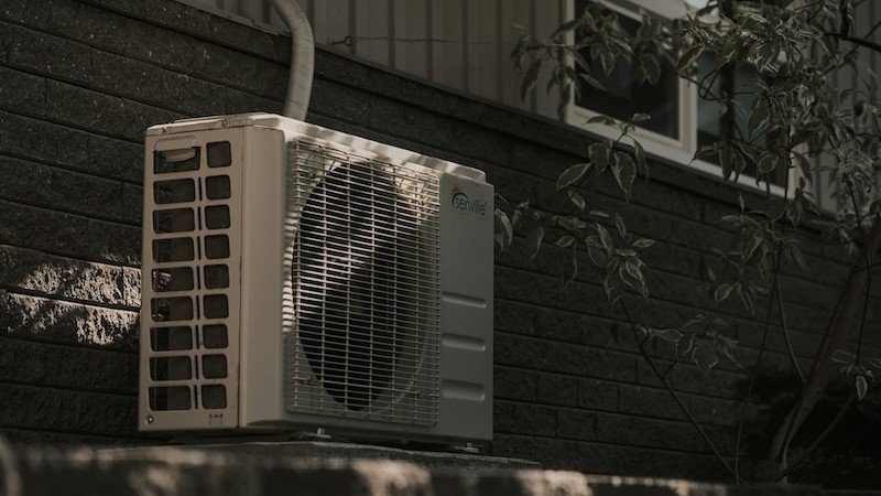A residential heat pump unit mounted on the exterior wall of a home
