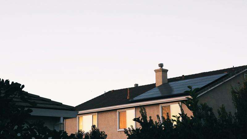 A California suburban home at dusk with solar panels installed on the roof and warm light glowing through the windows.