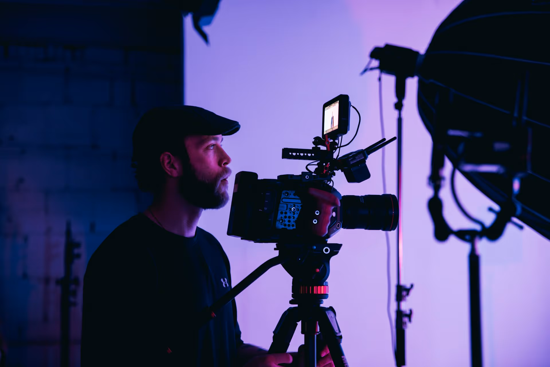 Man operating a professional video camera on a tripod in a studio with purple lighting.
