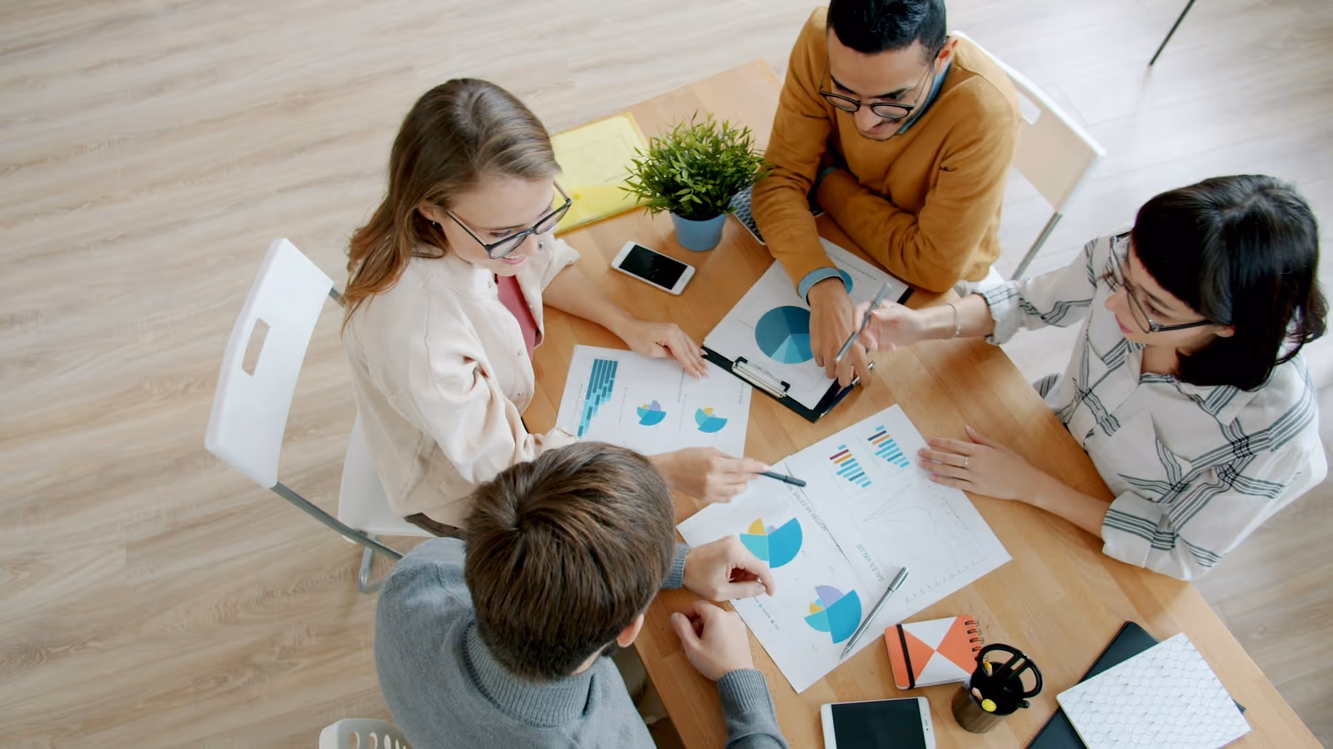 Four people sitting around a wooden table reviewing colorful charts and graphs during a meeting.